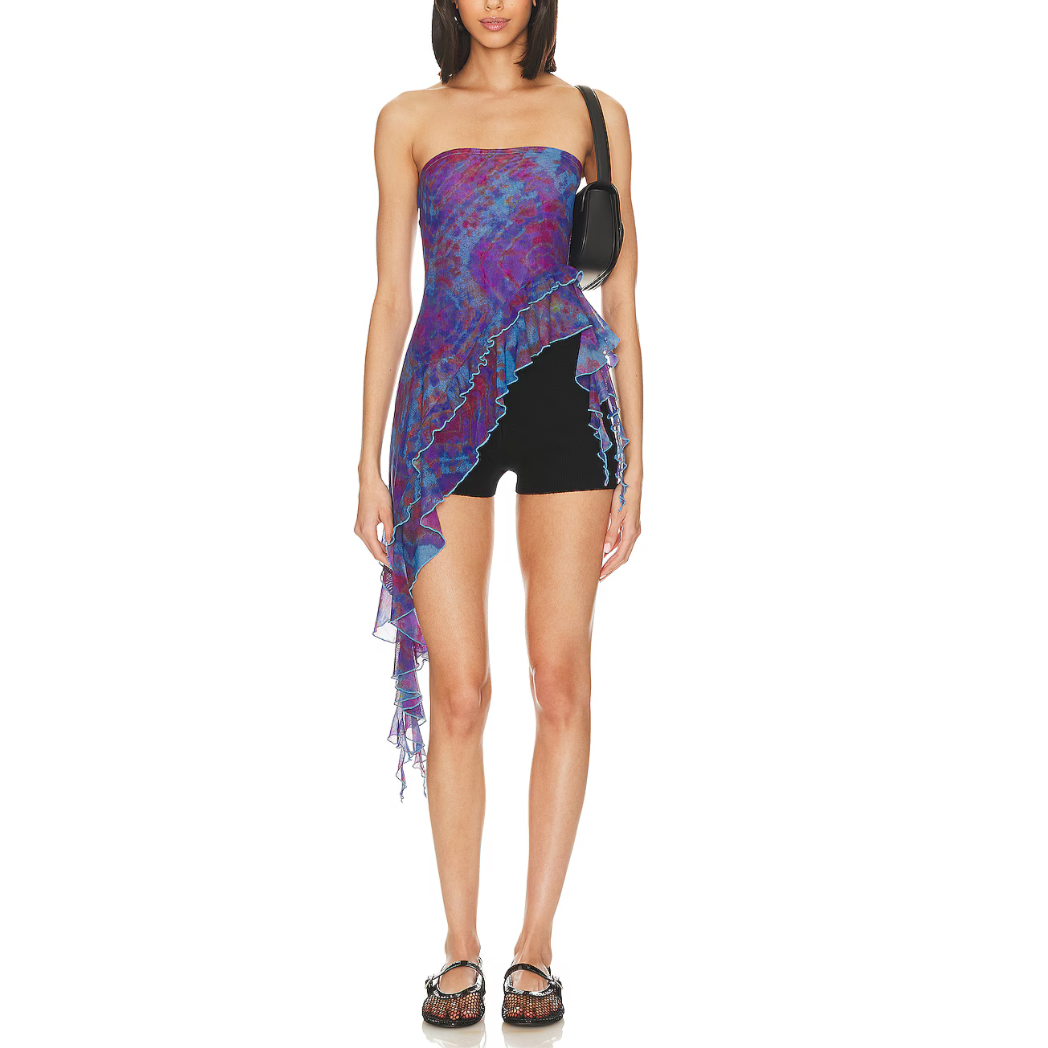 A female model wearing a blue and purple floral tube top with asymmetric draped ruffle sides, paired with black shorts and sunglasses.