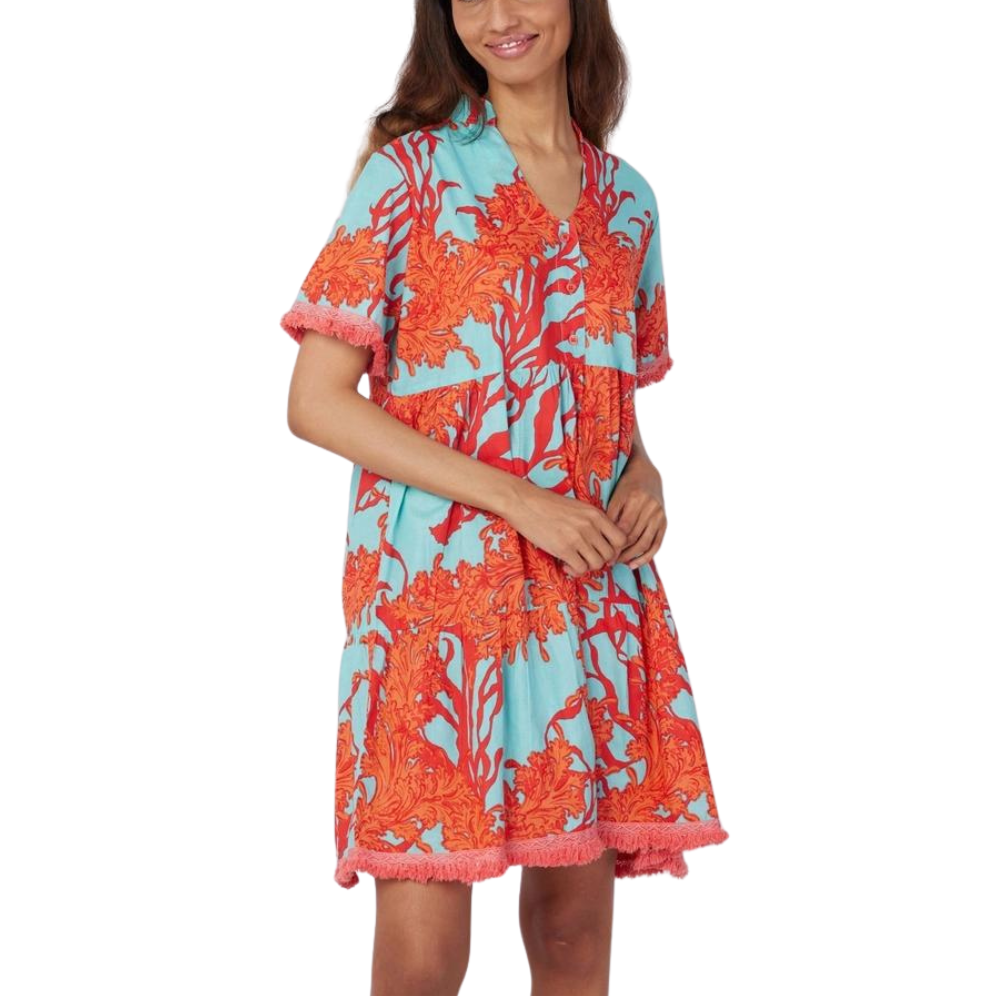 A woman wearing a knee-length cotton dress with a tropical blue and red coral motif, and fringe trim on the sleeves and hem.