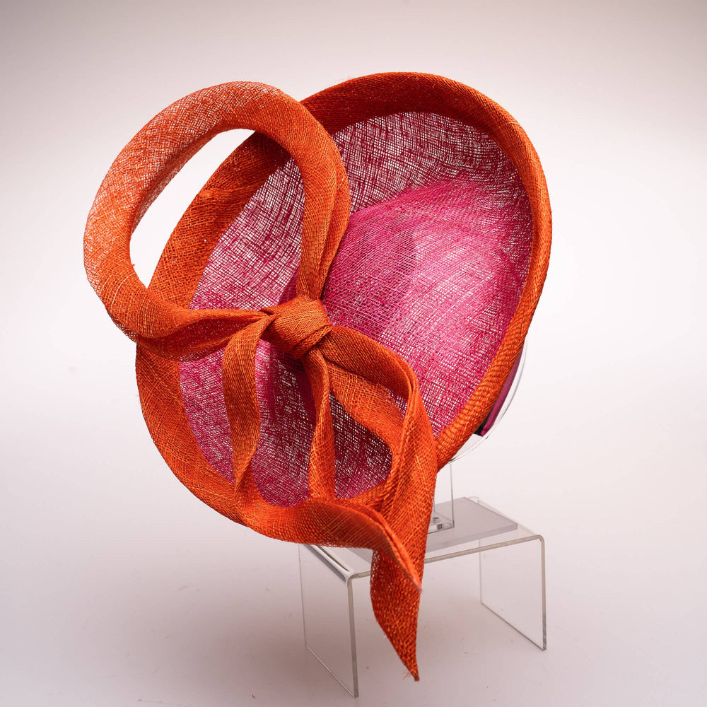 Orange and pink woven hat on a clear stand against a white background