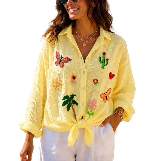 Woman wearing a yellow embroidered shirt on a beach with ocean and buildings in the background