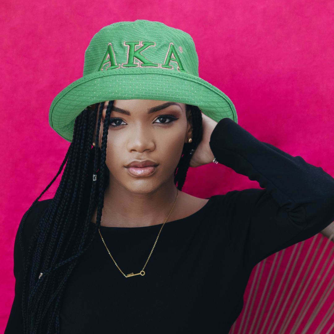 Person wearing a green 'AKA' hat against a pink background