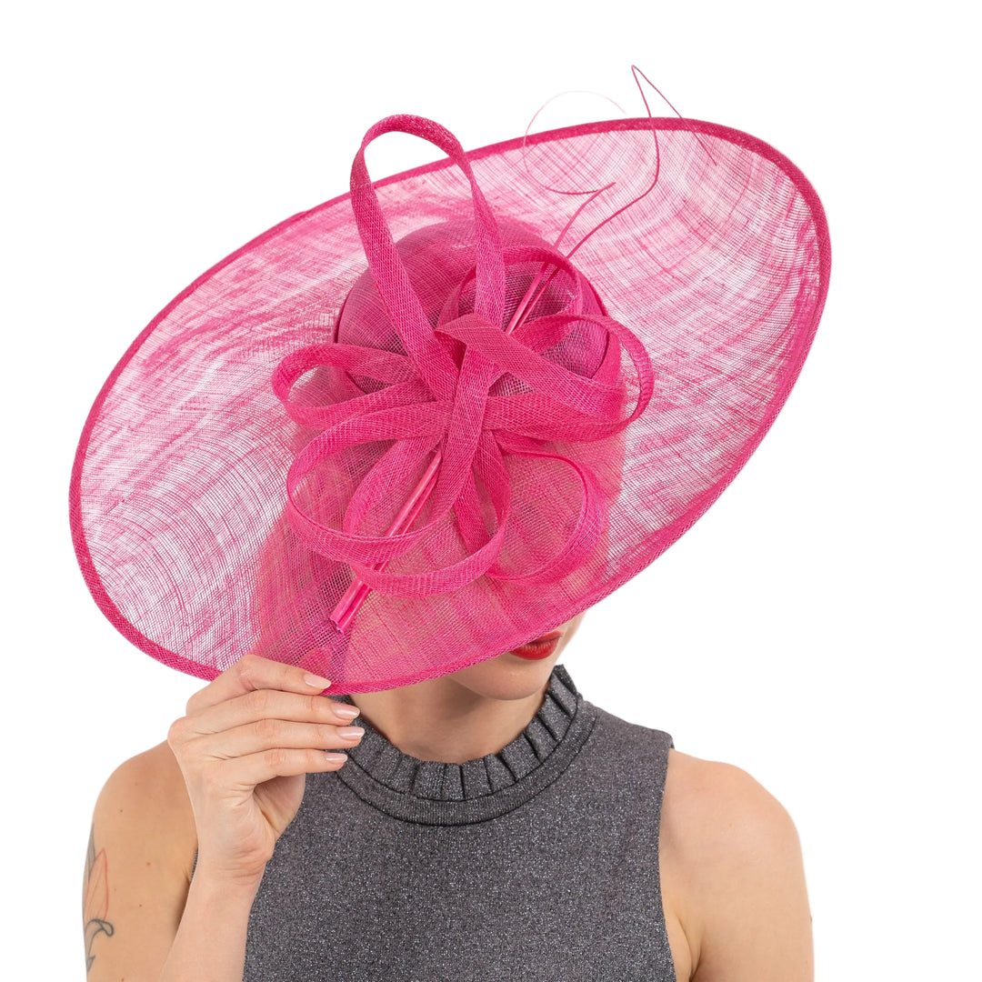 Person wearing a large pink hat with decorative ribbons on a white background