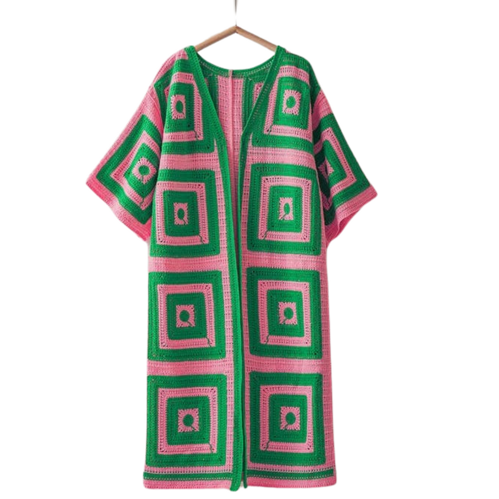 Green and pink crocheted cardigan on a hanger against a white background