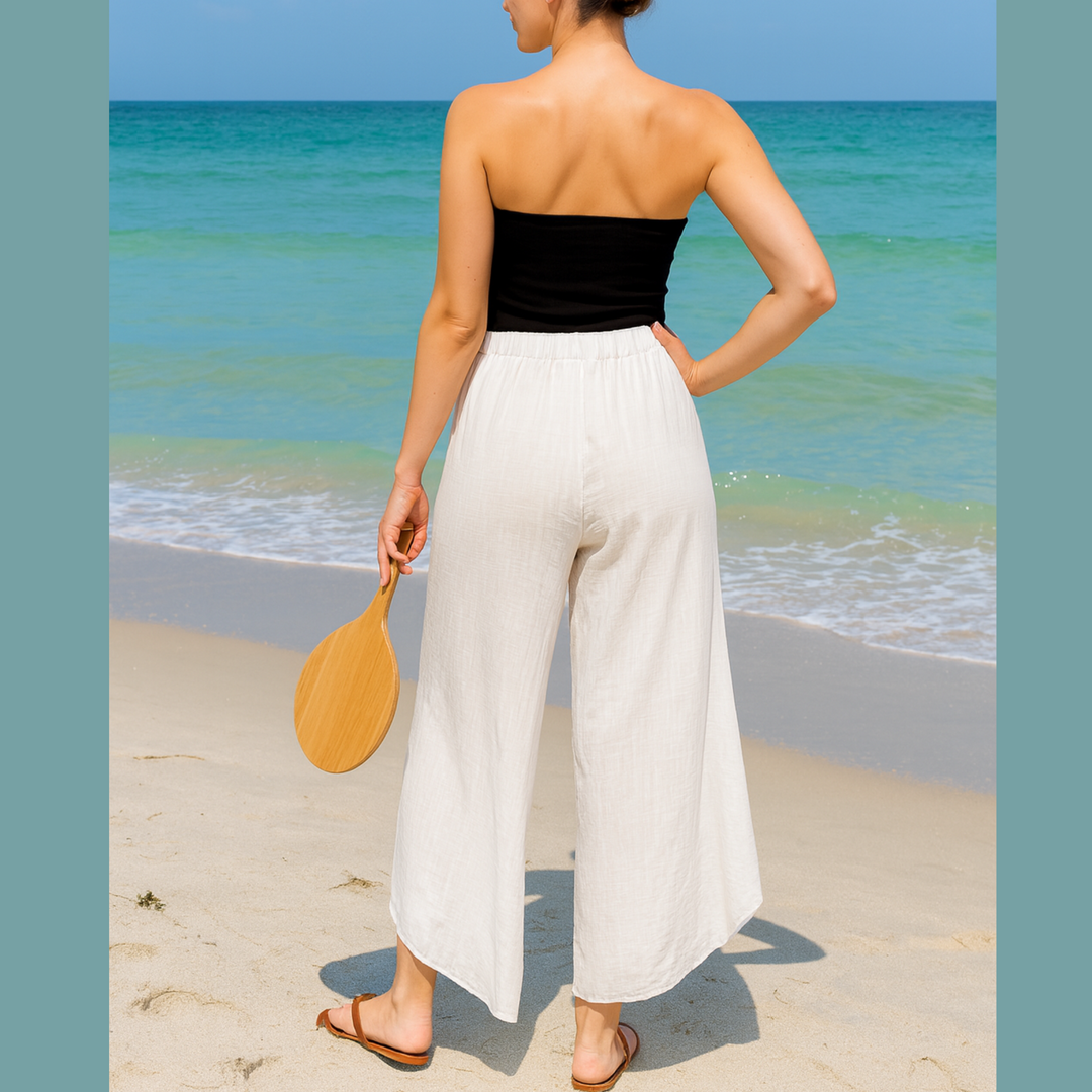 Woman in black top and white pants standing on a beach with ocean view