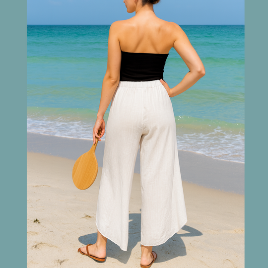 Woman in black top and white pants standing on a beach with ocean view