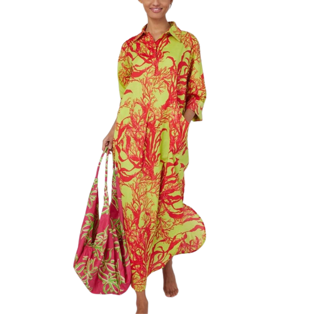 A woman wearing a maxi dress with a pink, green, and coral abstract print. The dress features a collar and front pockets, and appears to be made of a lightweight woven fabric.