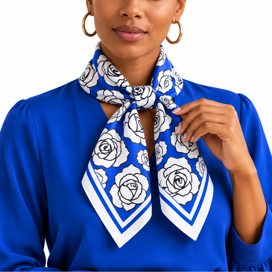 A woman wearing a royal blue blouse and a matching blue and white rose-patterned silk scarf, styled with gold hoop earrings against a solid white background.
