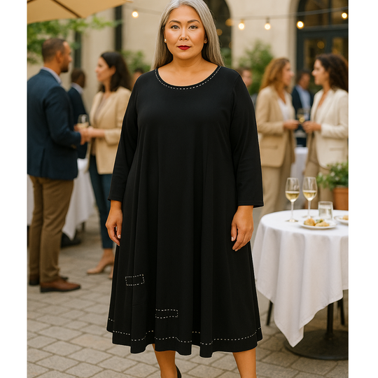 Woman in a black dress standing outdoors at an event with people and tables in the background.