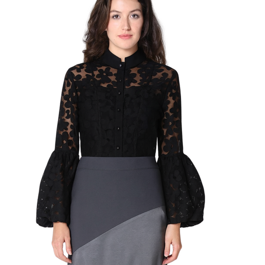 Woman wearing a black blouse with sheer sleeves and a gray skirt on a white background