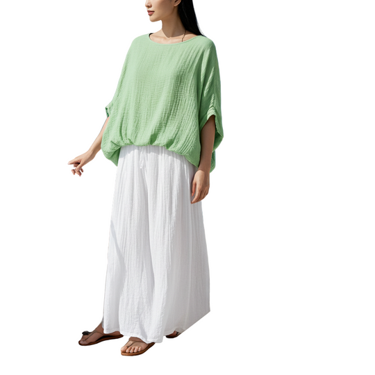 Woman in a green top and white pants standing on a boat with blue ocean in the background