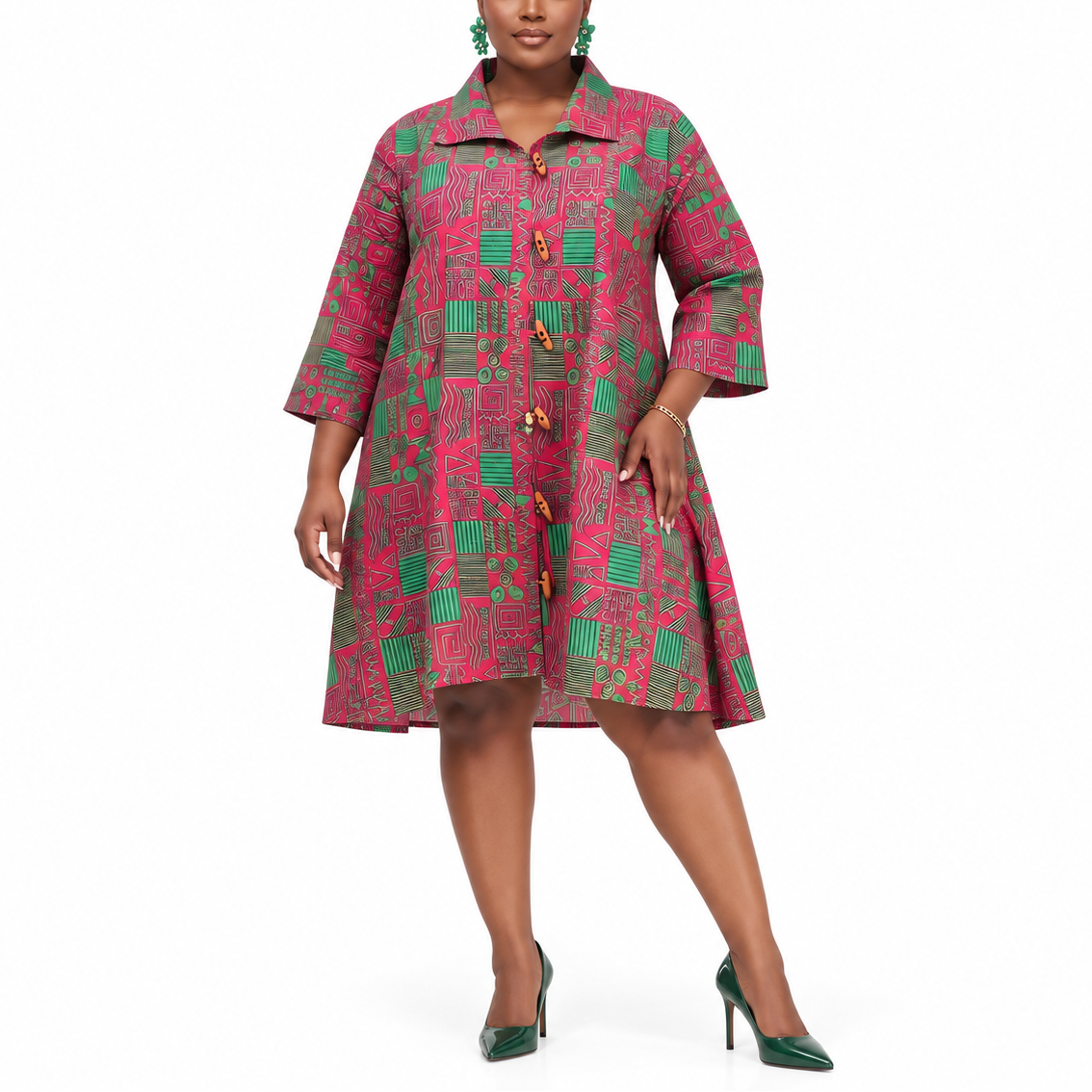 A woman modeling a short, button-front dress with three-quarter sleeves in a pink and green geometric pattern, paired with green high heels against a plain white background.