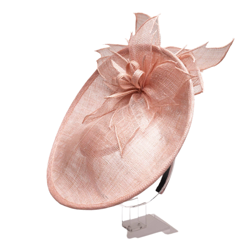 A light pink sinamay fascinator with a floral pattern on the top and a plain base. The fascinator features a side shelf or platform and is positioned on a mannequin head.