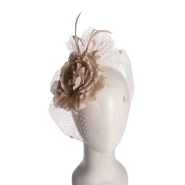 A beige fascinator hat featuring a large fabric flower and delicate netting veil, displayed on a white mannequin head against a light gray background.
