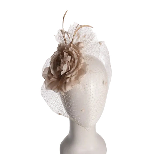 A beige fascinator hat featuring a large fabric flower and delicate netting veil, displayed on a white mannequin head against a light gray background.