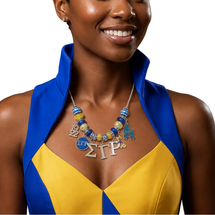 A smiling woman with short curly black hair is shown from the chest up at an indoor event. She wears a bright blue and yellow halter-style dress and a chunky beaded necklace with Greek letter charms.