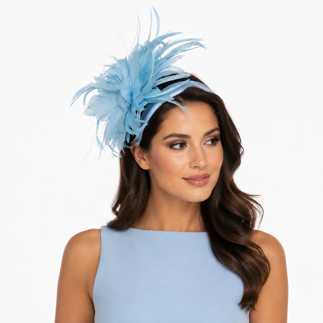 A woman wearing a light blue feather fascinator headpiece on a black headband, paired with a matching light blue sleeveless top, against a plain white background.