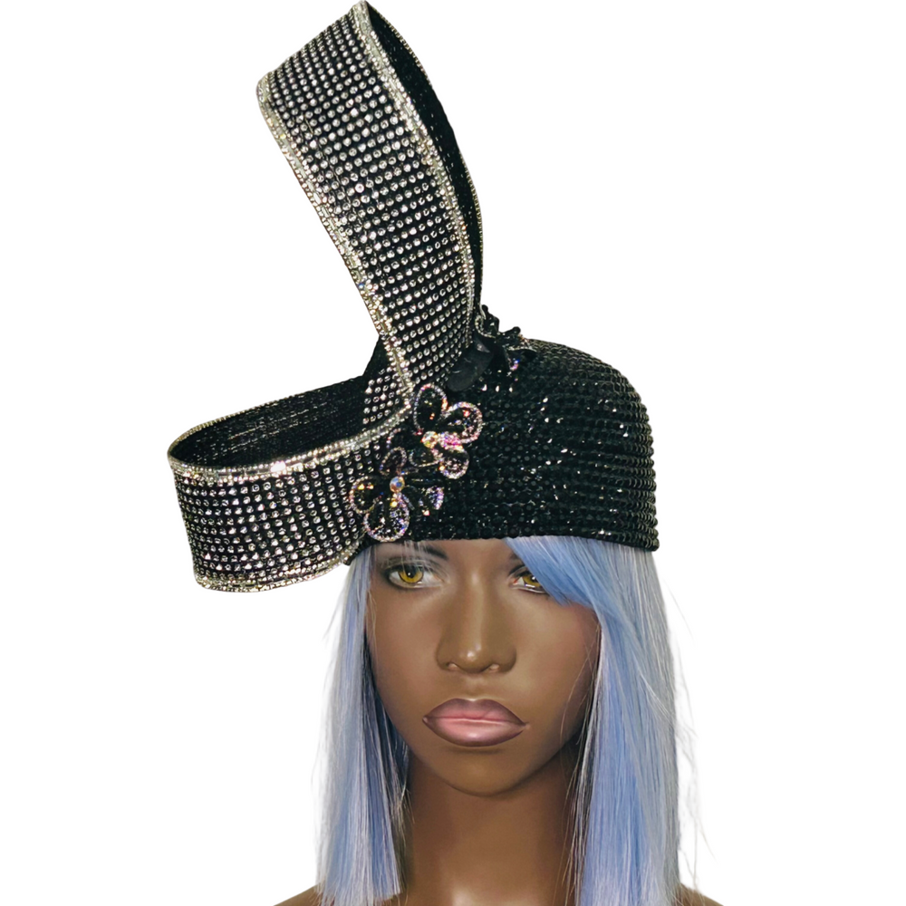A black crystal-laden bubble hat with a floral design and a dramatic swirl, worn by a mannequin with blue hair.