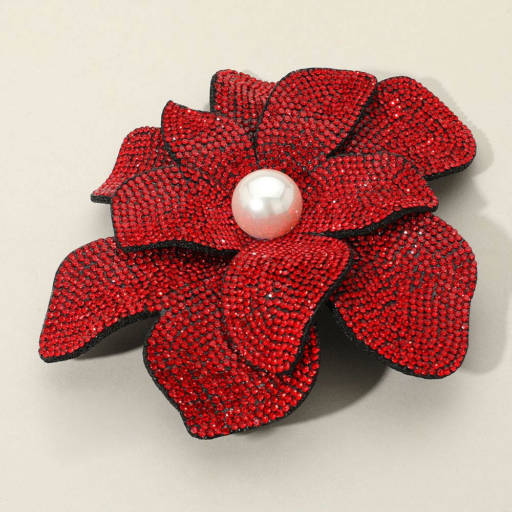 Red flower-shaped brooch with a pearl center on a beige background