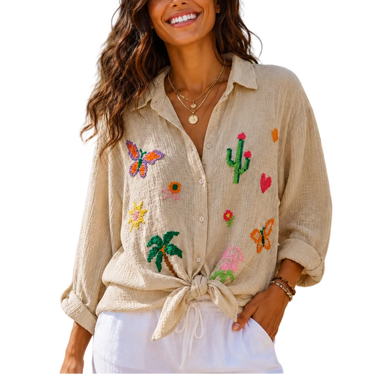 Woman wearing a beige embroidered shirt on a beach with ocean and palm trees in the background