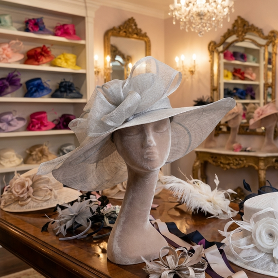 Mannequin head with a large decorative hat in a room with shelves of hats and mirrors.