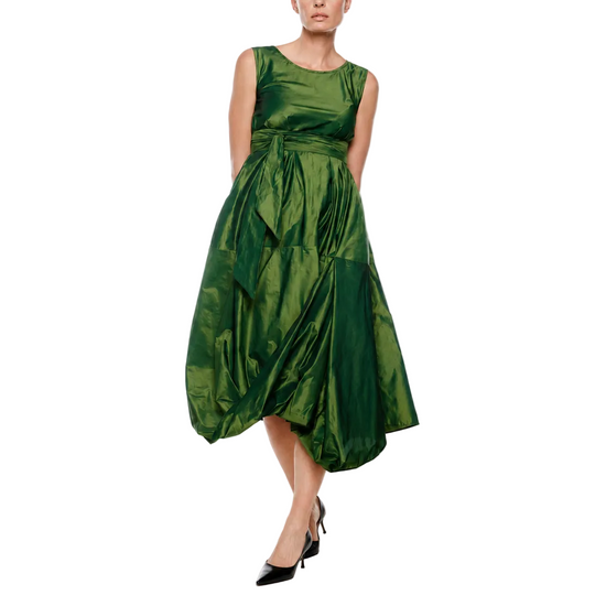 A woman modeling a sleeveless, mid-length green dress with a gathered, voluminous skirt and black pointed-toe heels, photographed against a seamless white studio background.