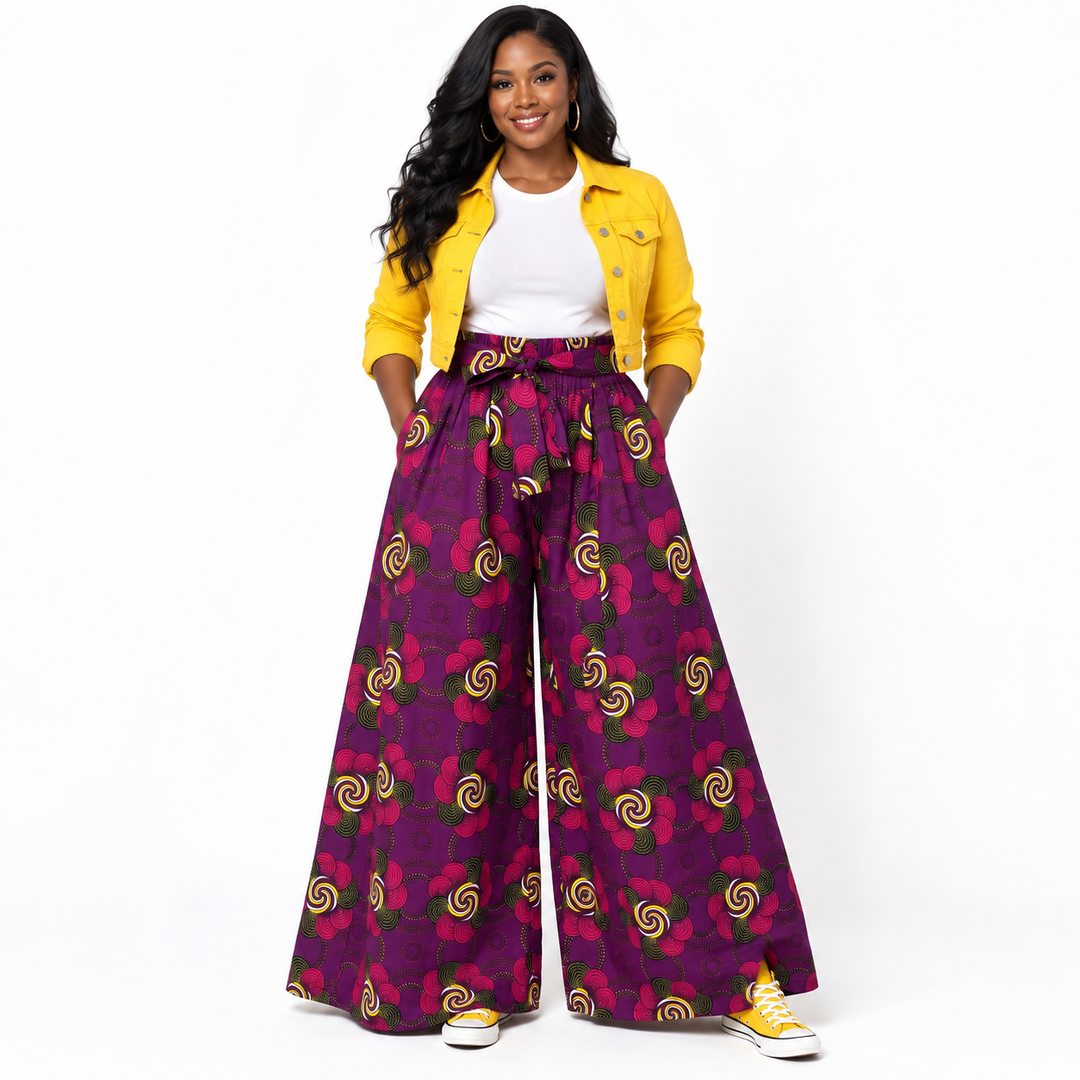 A woman modeling high-waisted, wide-leg trousers with a purple and magenta floral pattern, styled with a yellow jacket, white t-shirt, and yellow sneakers against a white studio background.