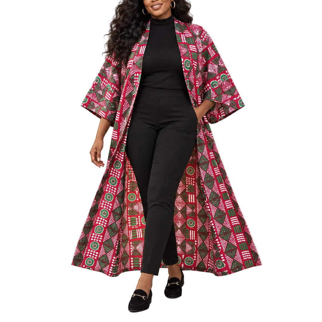 A woman modeling a long open-front kimono-style coat with wide three-quarter sleeves, featuring a vibrant pink, red, green, and black geometric African wax print. She is styled with a black turtleneck, black pants, and black loafers against a solid light gray studio background.