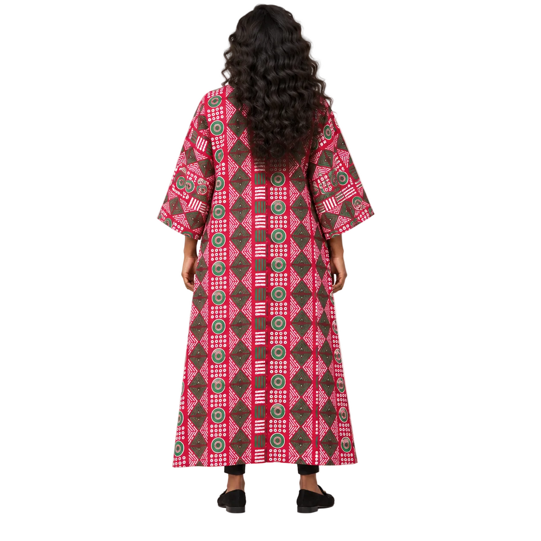 A woman viewed from behind wearing a long, wide-sleeved kaftan dress with a vibrant pink, brown, and green geometric pattern, set against a plain light gray studio background.