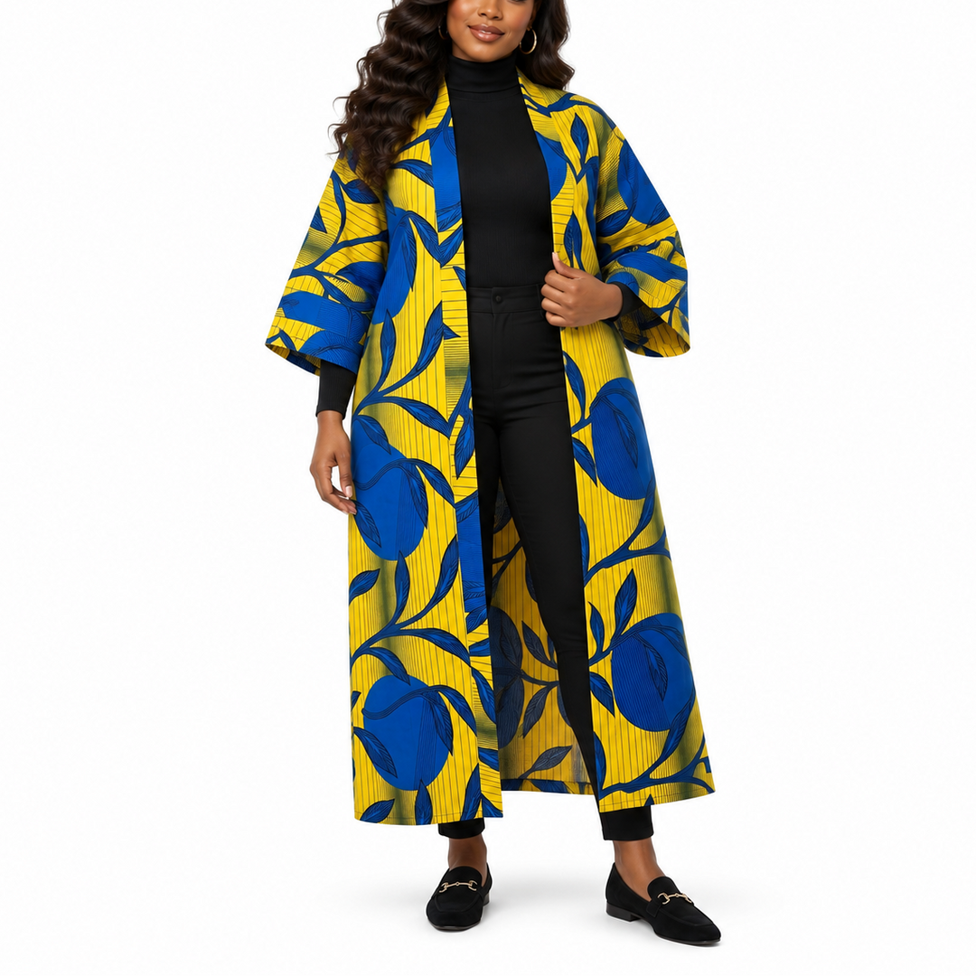 A woman modeling a long open-front coat with a bold blue and yellow floral print over a black outfit, photographed against a plain white studio background.