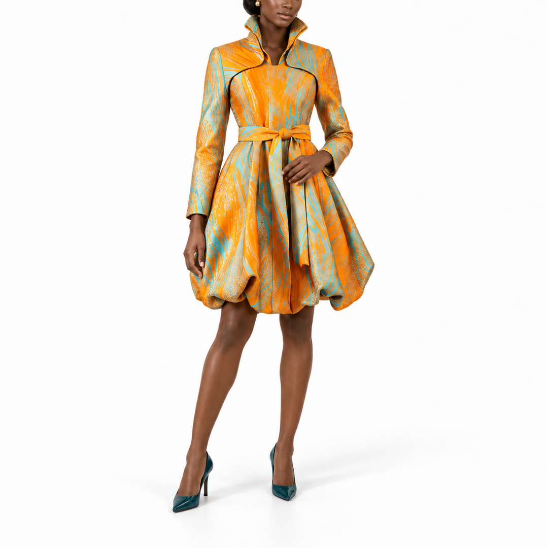 A model wears a short, long-sleeved dress with a high stand collar and a flared skirt, featuring an abstract orange, yellow, and teal pattern with thin black piping details. She is wearing teal high heels against a solid white studio background.