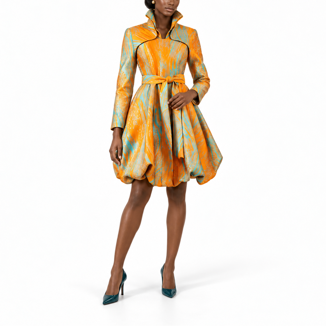 A model wears a short, long-sleeved dress with a high stand collar and a flared skirt, featuring an abstract orange, yellow, and teal pattern with thin black piping details. She is wearing teal high heels against a solid white studio background.