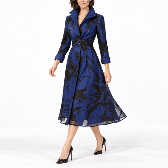 A woman modeling a blue and black patterned midi wrap coat dress with a waist tie, shown against a plain white studio background.