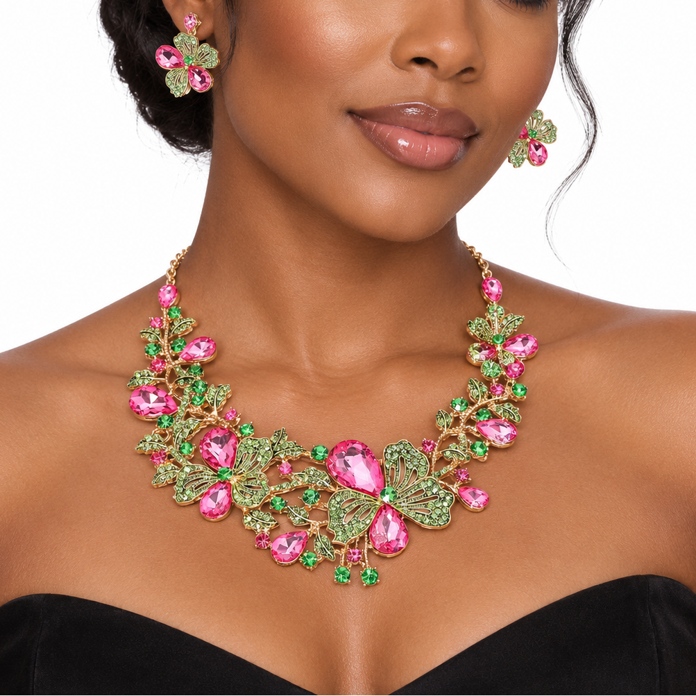 A woman wearing a pink and green rhinestone floral statement necklace with matching flower-shaped earrings, styled with a black strapless top against a white background.
