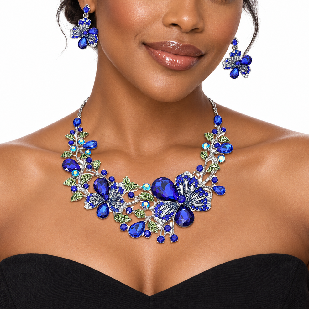 A woman wearing a blue and green floral statement necklace with matching drop earrings, shown against a plain white background.