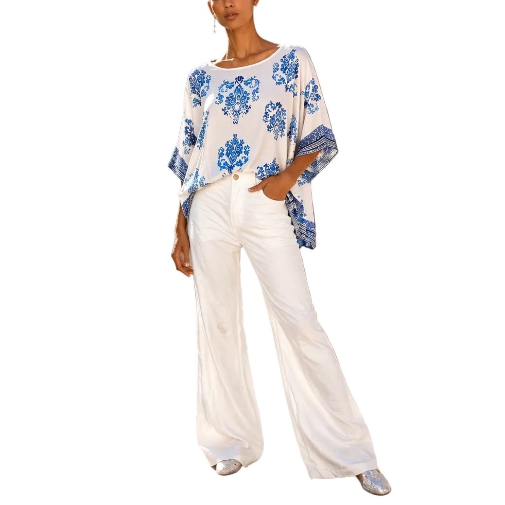 Woman in a floral top and white pants standing on a stone path with scenic background