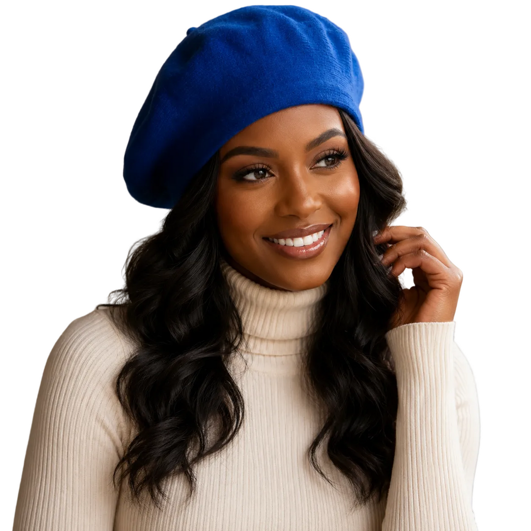 A smiling woman with long wavy black hair wears a bright royal blue beret and a cream ribbed turtleneck sweater against a warm beige studio background.