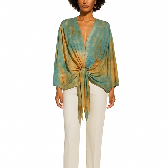 Woman wearing a green and gold patterned top with white pants on a white background