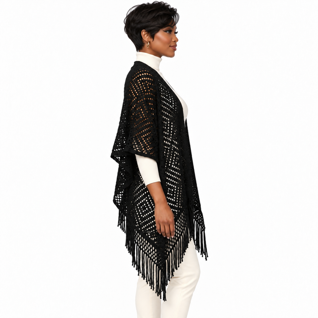 A woman shown in side profile wearing a black open-knit fringed poncho over a white mock-neck top and white pants, against a plain white studio background.