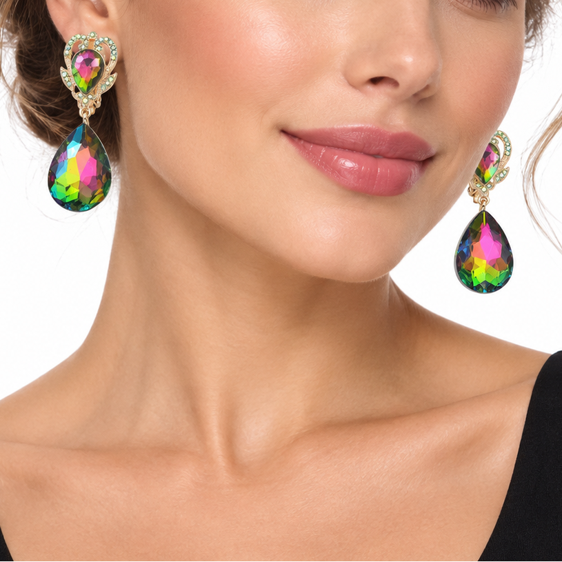 A close-up of a woman wearing a pair of dangling teardrop earrings with iridescent rainbow-colored stones and gold-toned settings, against a plain white background.