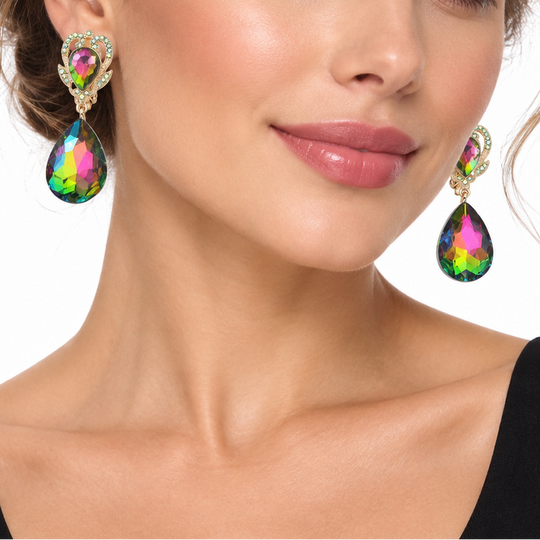 A close-up of a woman wearing a pair of dangling teardrop earrings with iridescent rainbow-colored stones and gold-toned settings, against a plain white background.