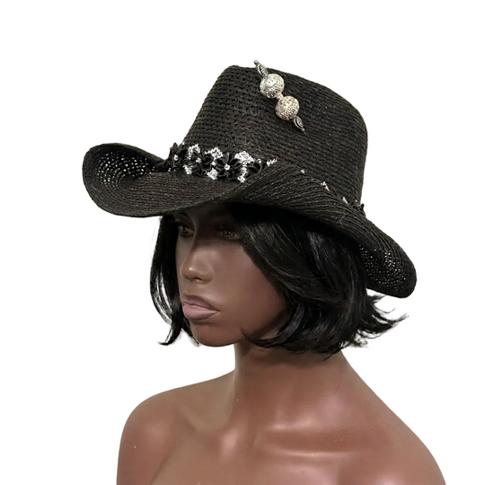 Black cowboy hat with decorative elements on a mannequin head against a beige background