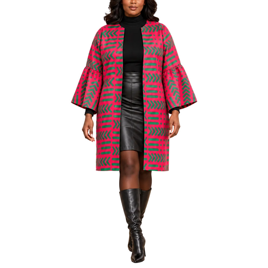 A woman models a vibrant pink and gray geometric patterned coat with flared bell sleeves, worn over a black turtleneck, black leather skirt, and black knee-high boots in a luxurious hotel lobby setting.