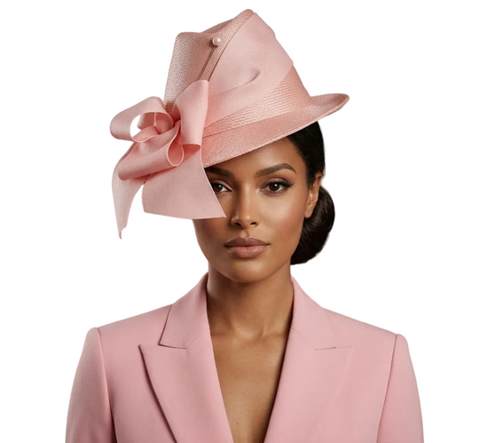Woman wearing a pink hat with a large bow and matching pink blazer against a neutral background.