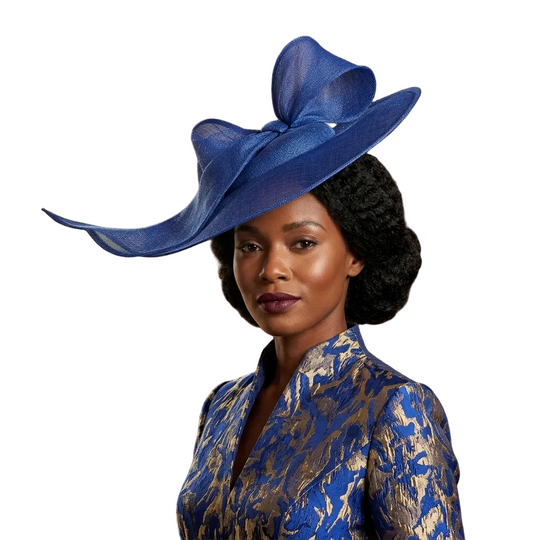 Woman wearing a blue and gold patterned outfit with a large blue hat in a room with wooden paneling and a window.
