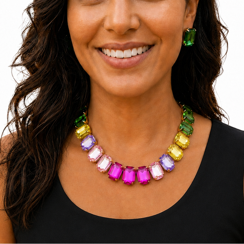 A smiling woman with long dark hair wearing a colorful gemstone necklace and matching green earrings, photographed against a plain white background.