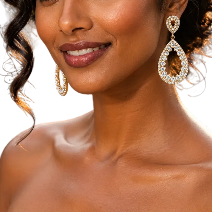 A woman in a formal evening gown wearing large teardrop-shaped diamond-studded earrings, photographed outdoors at night with blurred guests and string lights in the background.