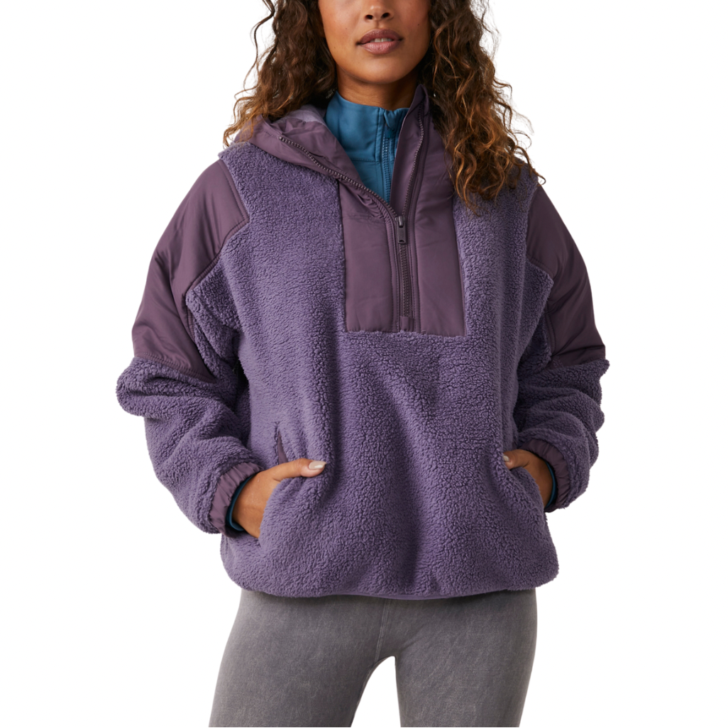 A woman wearing a purple fleece pullover with a hood, featuring water-resistant woven patches and jersey-lined pockets.