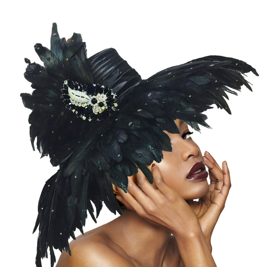 A close-up image of a woman wearing a black feathered brim hat with a luxurious brooch on top.