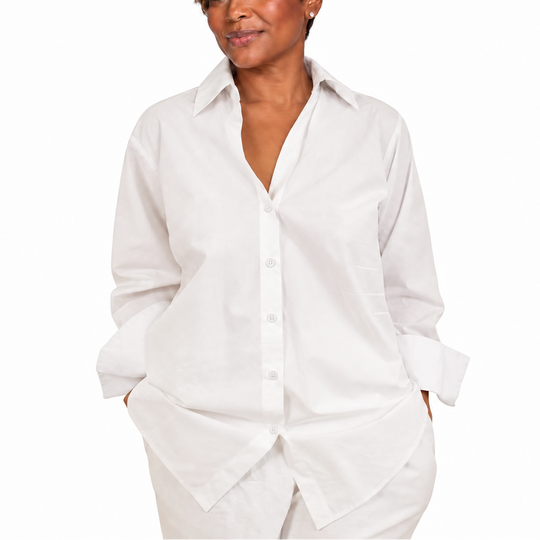 A woman modeling a white long-sleeve button-down shirt with a relaxed, oversized fit, paired with matching white pants, against a solid white background.