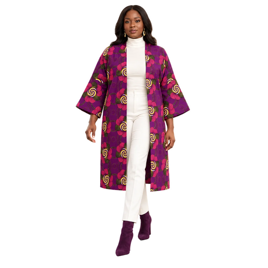 A woman walks through a modern, upscale lobby wearing a vibrant purple and magenta patterned open-front coat over a white mock-neck top and white pants, paired with matching purple ankle boots.